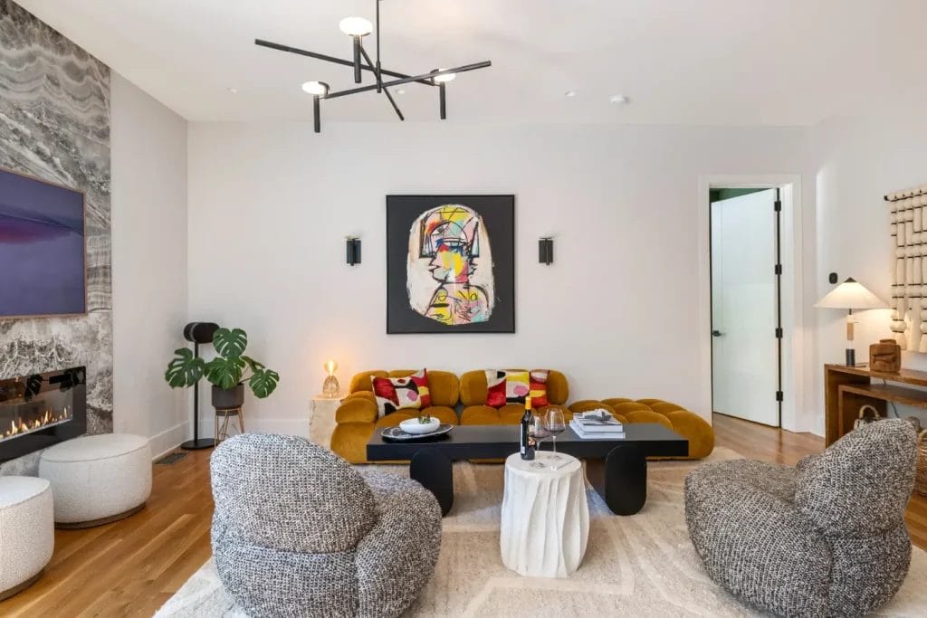 Modern living room shot by a str photographer featuring a mustard yellow sofa, textured gray chairs, abstract wall art, black coffee table, white accent table, fireplace, plants, and decor on wood flooring with a light rug.