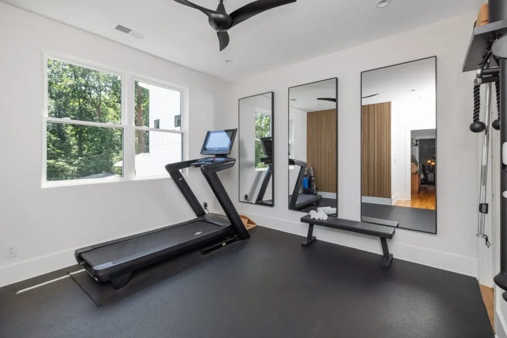 A modern home gym, perfect for a str photographer, with a treadmill facing a window, bench and dumbbells, three large mirrors on the wall, white walls, black flooring, and a ceiling fan above to keep you cool during workouts or shoots.