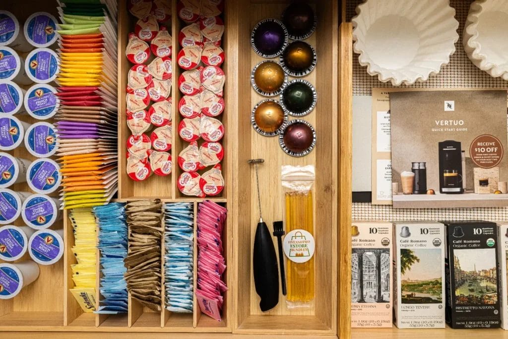 A neatly organized kitchen drawer holds coffee capsules, tea bags, sugar packets, honey sticks, coffee creamers, coffee filters, and Nespresso Vertuo promotional materials—ready for any str photographer seeking the perfect shot.