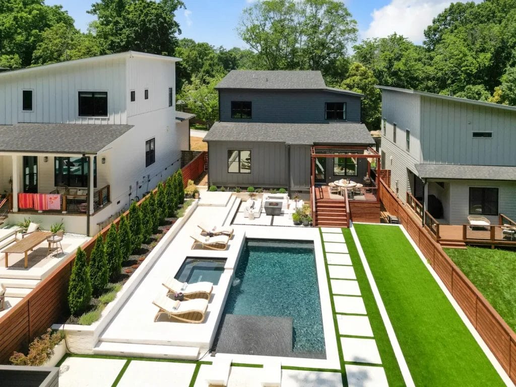A modern backyard with a rectangular swimming pool, lounge chairs, patio seating, and neatly landscaped green grass is beautifully captured by an str photographer, surrounded by contemporary houses and wooden fences.