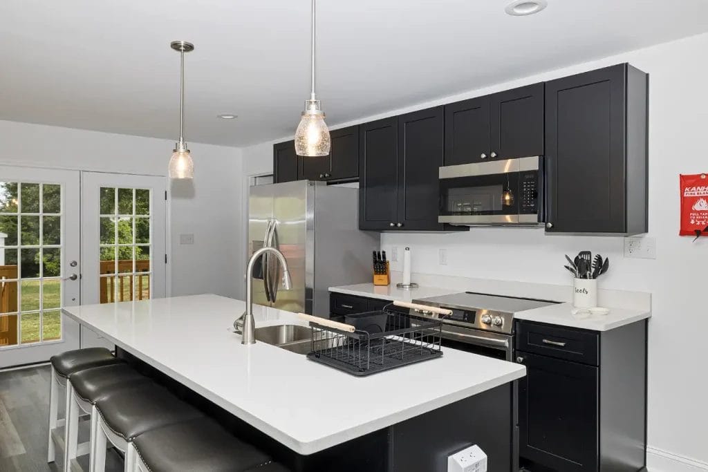Modern kitchen with black cabinets, white countertops, stainless steel appliances, a center island with bar stools, pendant lights, and French doors leading outside.