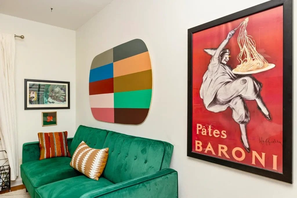 A living room with a green velvet couch, two patterned pillows, colorful geometric wall art, and a vintage “Pâtes Baroni” poster—perfectly captured by an Artistic Photographer in Charlotte NC for your next Airbnb listing.