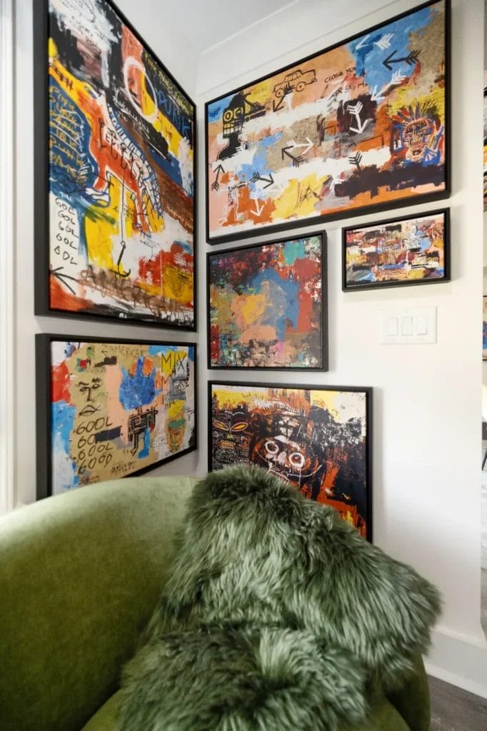 A green faux-fur chair sits in the corner of a room with colorful abstract art, reminiscent of Jean-Michel Basquiat’s style, displayed on the white walls in black frames.