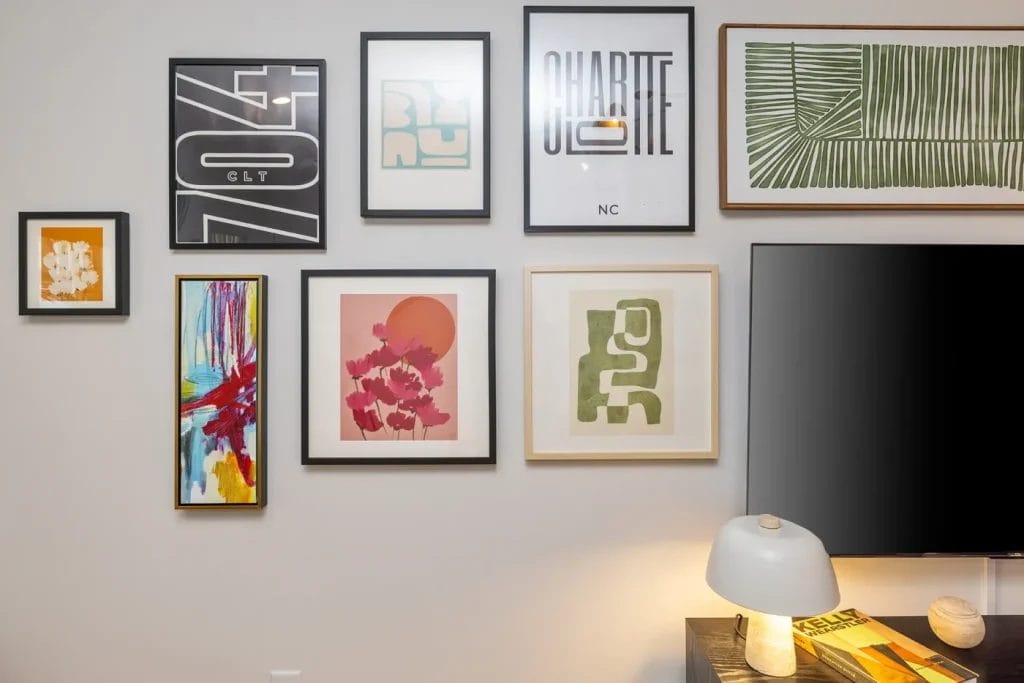 A gallery wall displays a variety of framed abstract art pieces in different sizes and colors above a lamp and a TV on a modern console table.