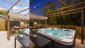 Outdoor patio with wooden pergola, dining table, string lights, potted plants, and a hot tub, surrounded by a wooden privacy fence and trees in the background under a partly cloudy sky.